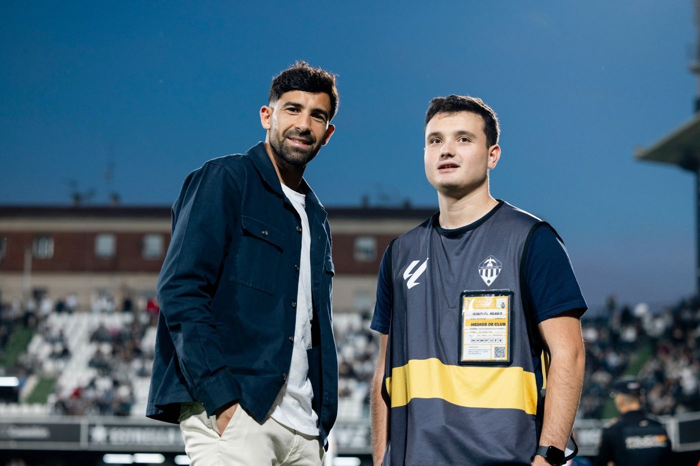 Kiko con el peto de medios de club del CD Castellón junto a un jugador sobre el césped